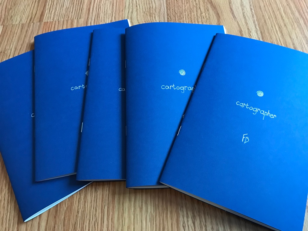 A photo of the booklets. the covers are blue cardstock with white lettering. they each bear a spiral, the word "cartographer", and my initials—"FB".